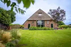 Achtergevel van de Sallandse boerderijwoning met rieten dak, grote raampartij en landelijke tuin in Okkenbroek.