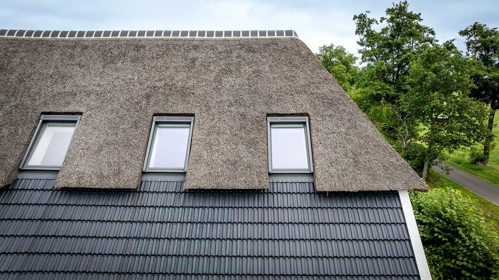Detail van het rieten en pannendak met dakramen; kenmerkend voor de vernieuwde boerderij in Okkenbroek.