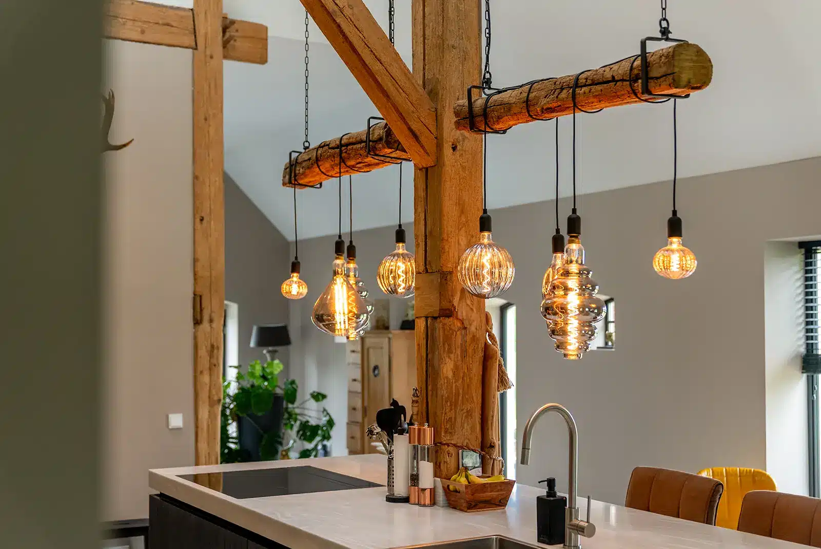 Detail van de verlichting aan de houten balken boven het kookeiland; een sfeervol accent in de boerderij in Okkenbroek.
