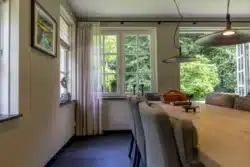Eethoek met klassieke raampartijen en warme lichtinval; uitbouw in harmonie met de stijl van de jaren ’20 villa.