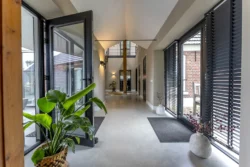 Entree van de verbouwde boerderij in Okkenbroek met zwarte deuren en een lichte hal waar oud en nieuw mooi samenkomen.