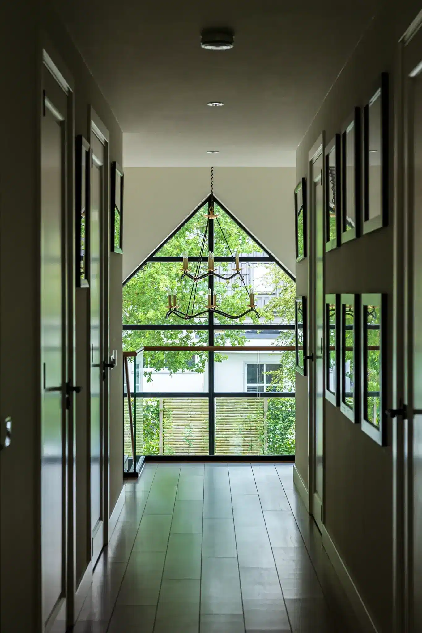 Doorkijk vanaf de overloop naar de vide met grote puntgevelramen en kroonluchter in Wesepe.