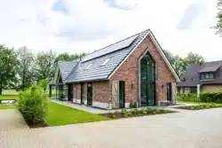 Voorgevel met traditionele baksteen, hoge glaspartij en zonnepanelen, gezien vanaf de oprit in Wesepe.