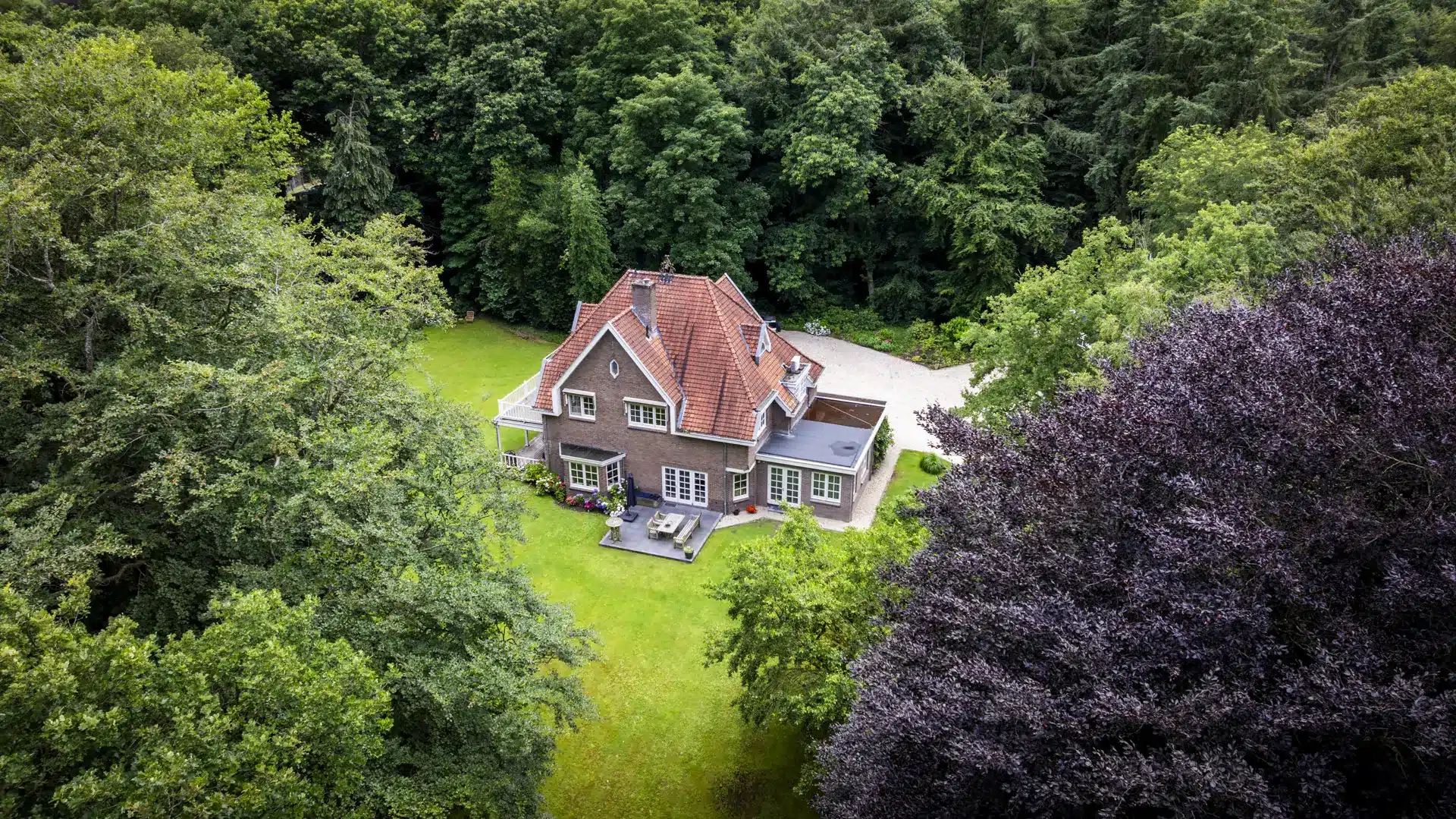 Luchtfoto van de uitgebouwde villa met rode dakpannen en groene tuin; een stijlvol geheel van oud en nieuw.