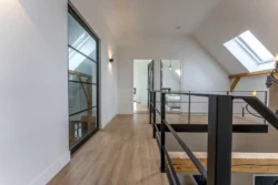 Overloop met stalen leuningen, veel lichtinval en zicht op de houten constructie van de boerderij in Okkenbroek.