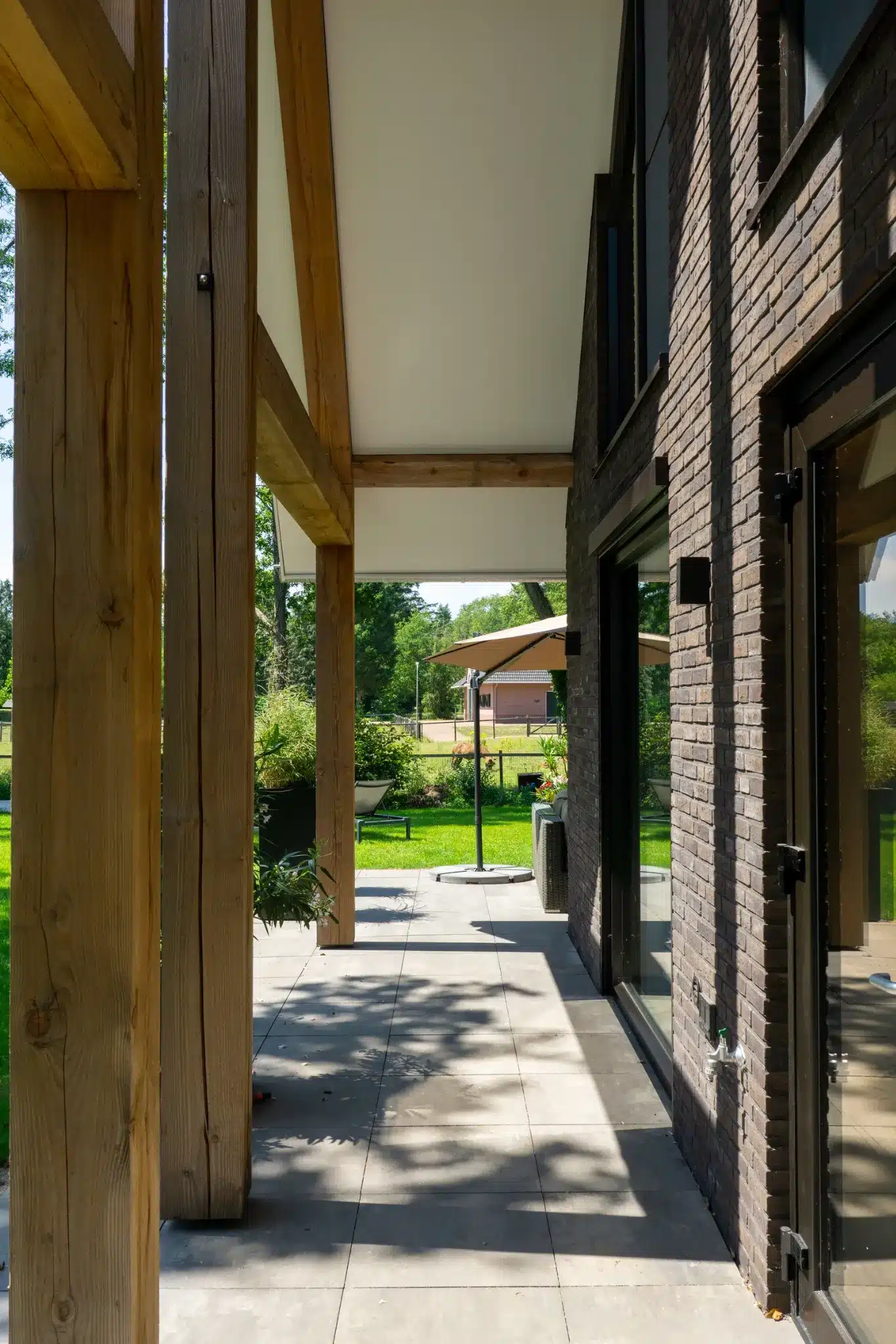 Overstek met houten gebinten en uitzicht op de groene tuin in Wesepe.
