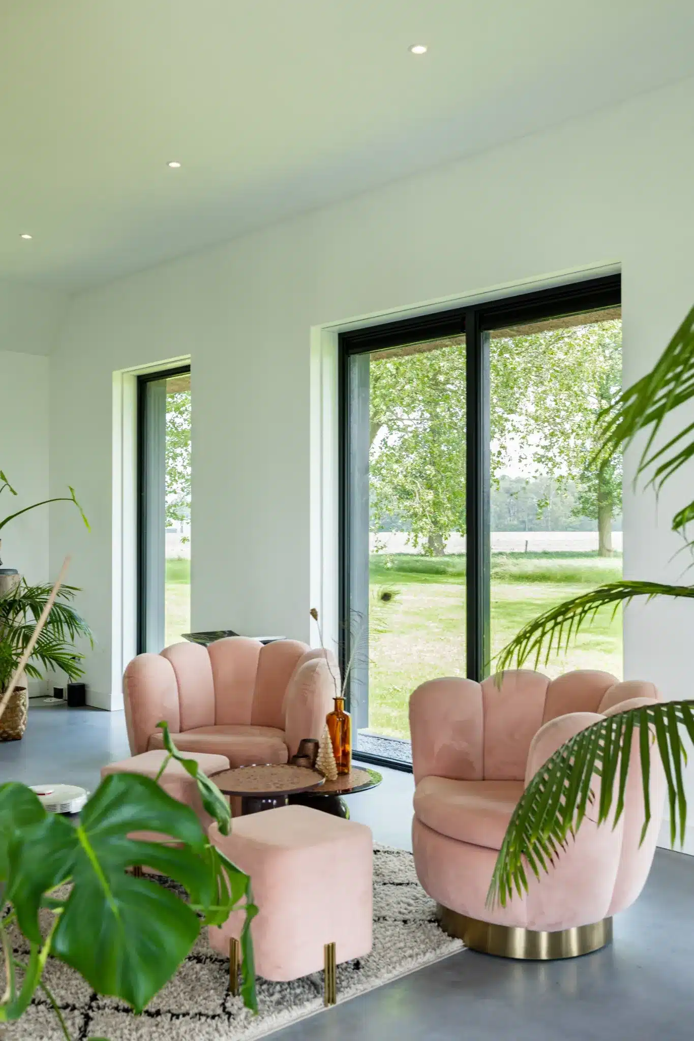 Zitkamer in de gerenoveerde boerderij met roze fauteuils en grote raampartijen die uitkijken over het omliggende landschap.
