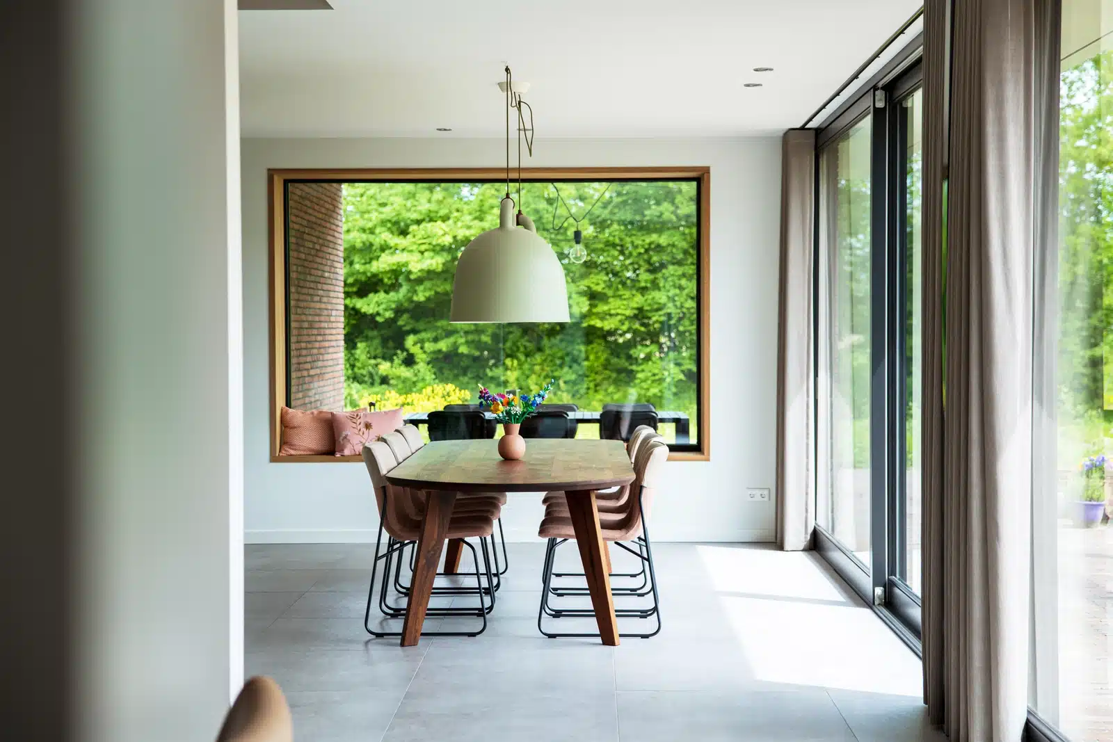 Lichte eetkamer met houten tafel, grote raampartijen en uitzicht op het groen bij de nieuwbouwwoning in Wesepe.