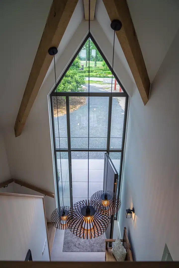 Vide boven de entree van een schuurwoning in Holten met hoge glazen pui, houten spanten en designverlichting die de ruimte verbindt met buiten.